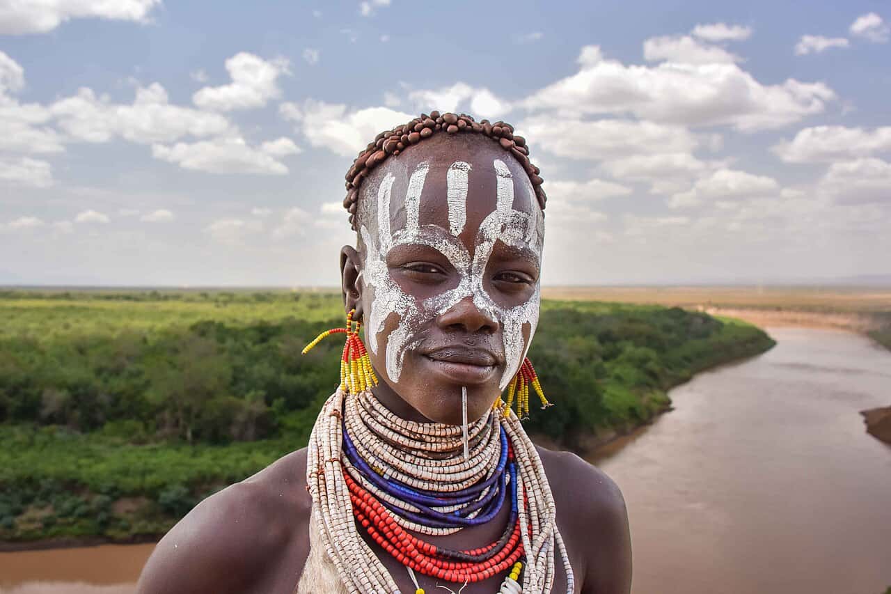 Portrait of a Karo woman with painted face and beaded necklaces, the Omo River behind her at Korcho